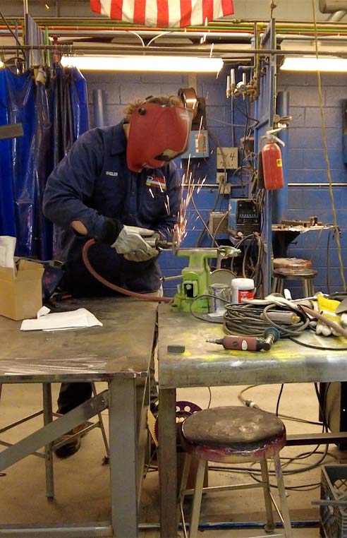 Student with welding gear on cutting metal